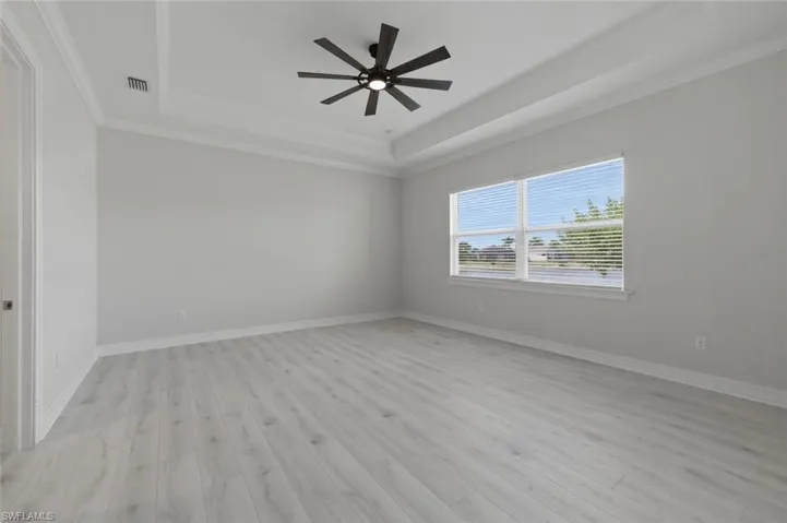 Empty room featuring a ceiling fan, crown molding, light wood-type flooring, and a raised ceiling