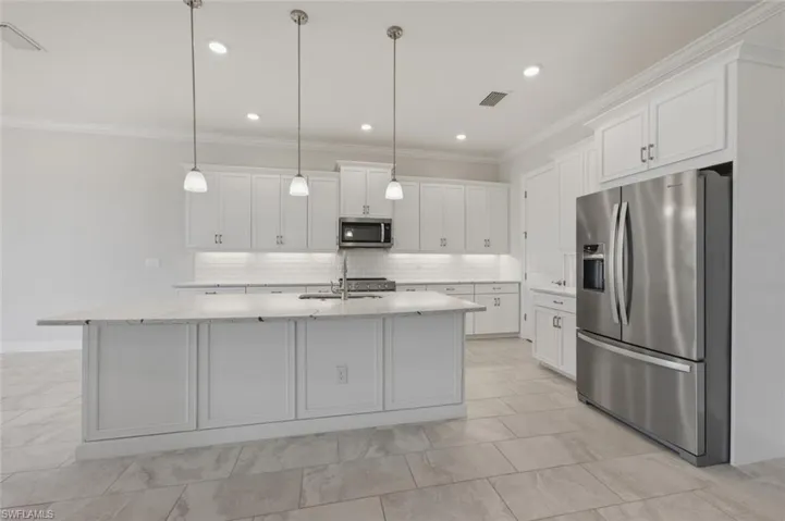 Kitchen featuring stainless steel appliances, backsplash, white cabinetry, crown molding, and light stone countertops
