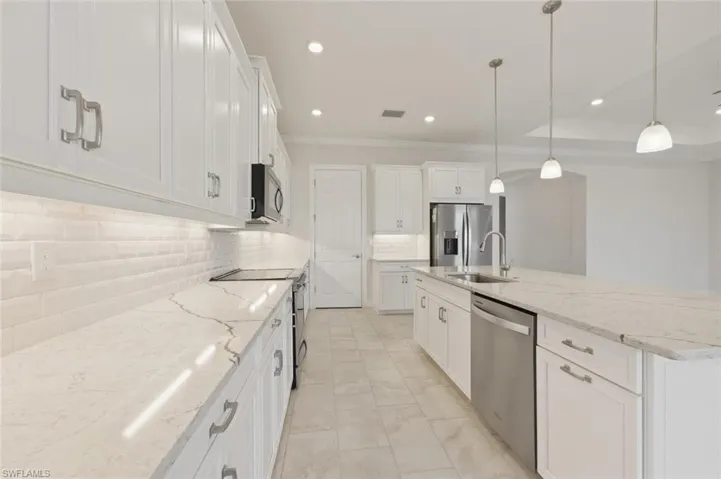 Kitchen featuring white cabinetry, light stone countertops, stainless steel appliances, and ornamental molding