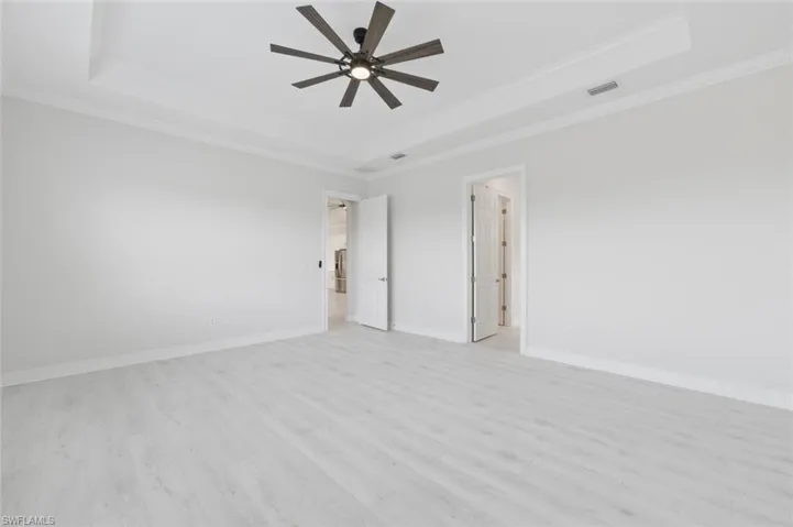 Unfurnished bedroom with light wood finished floors, ceiling fan, a tray ceiling, and crown molding