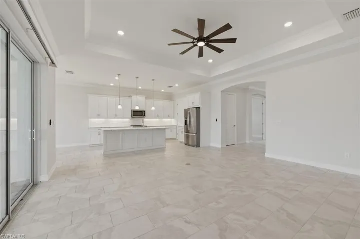 Unfurnished living room with arched walkways, crown molding, ceiling fan, recessed lighting, and a tray ceiling