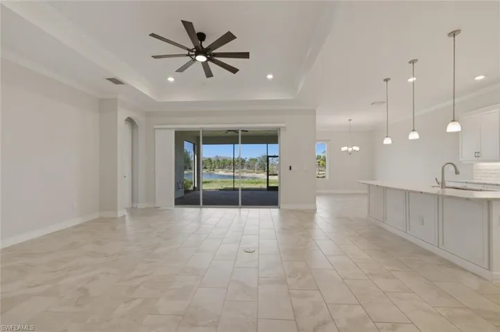 Unfurnished living room with a ceiling fan, a chandelier, crown molding, a raised ceiling, and a water view