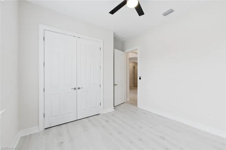 Unfurnished bedroom with arched walkways, light wood-style floors, ceiling fan, and a closet