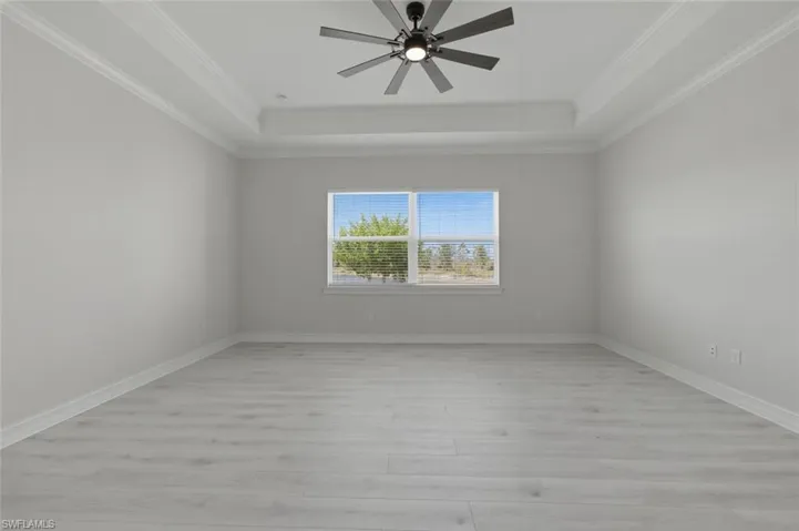 Spare room with light wood-style flooring, ceiling fan, a raised ceiling, and crown molding