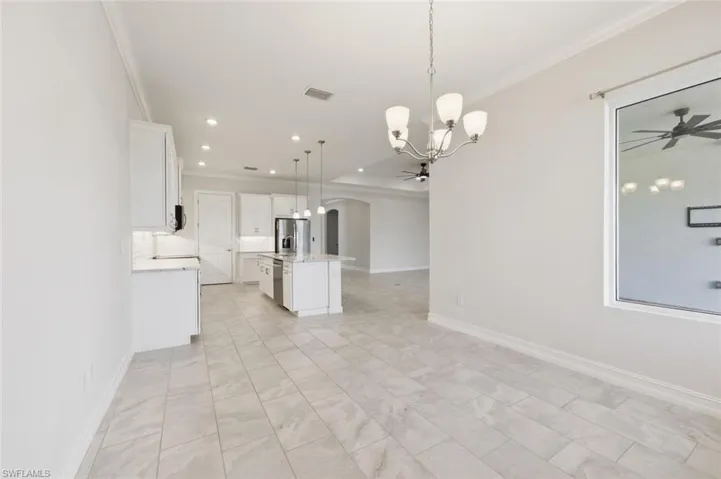 Kitchen with a ceiling fan, arched walkways, a chandelier, white cabinetry, and a center island with sink