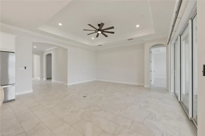 Empty room featuring arched walkways, crown molding, ceiling fan, recessed lighting, and a raised ceiling