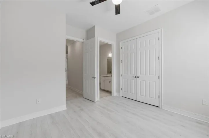 Unfurnished bedroom featuring light wood-style flooring, a closet, a ceiling fan, and connected bathroom
