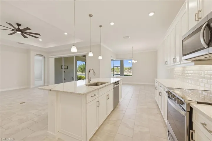Kitchen with white cabinets, stainless steel appliances, open floor plan, light stone counters, and a ceiling fan