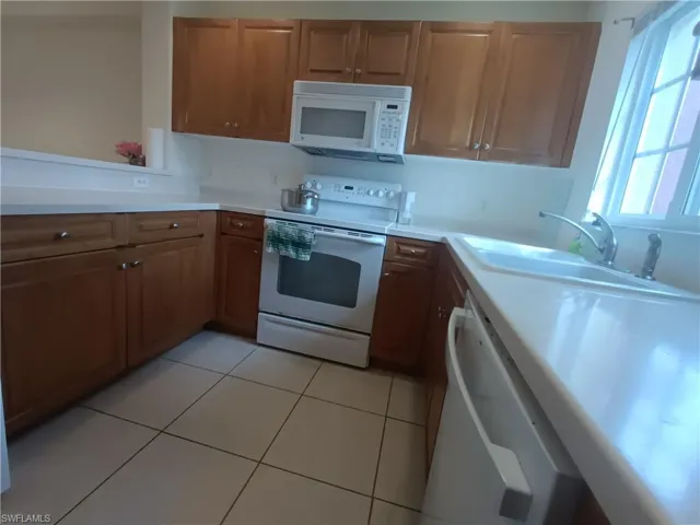 Kitchen with white appliances, light countertops, brown cabinetry, and light tile patterned floors