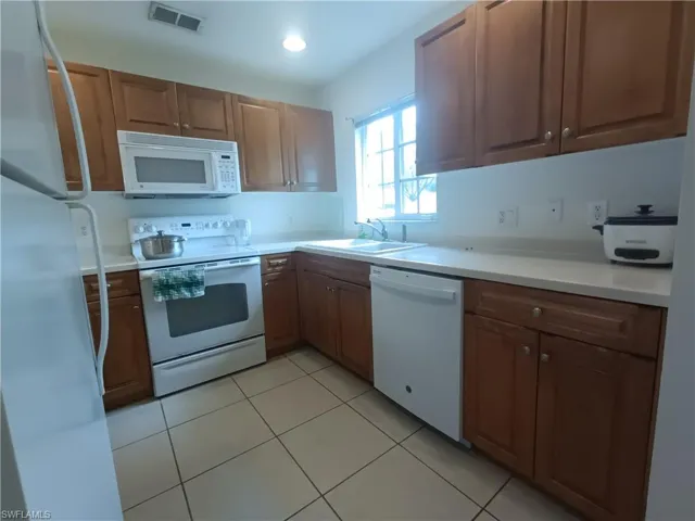 Kitchen featuring white appliances, light countertops, light tile patterned floors, and brown cabinetry