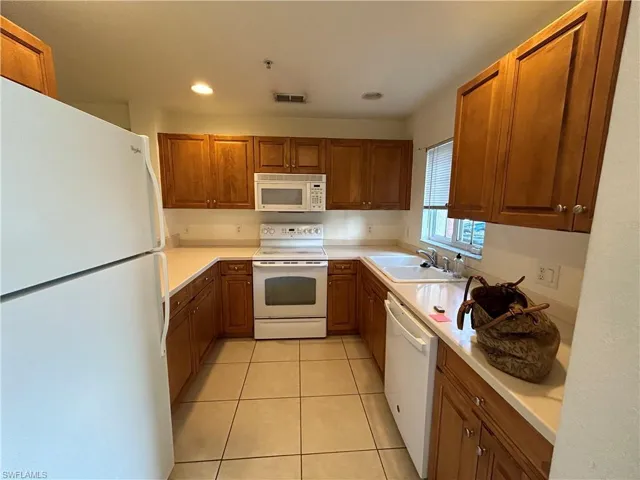 Kitchen featuring white appliances, brown cabinetry, light tile patterned floors, light countertops, and recessed lighting