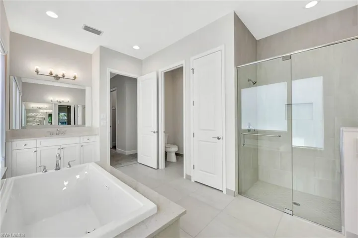 Primary bathroom with one of two vanities, plus walk in shower, toilet, and tile patterned floors