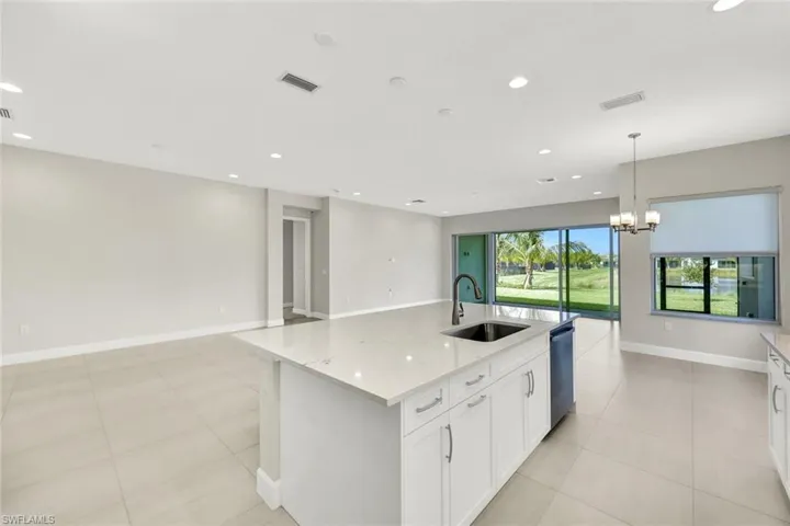 Kitchen with white cabinets, light stone countertops, a center island with sink, and a chandelier above Breakfast Area as well as views of Dining and Living areas