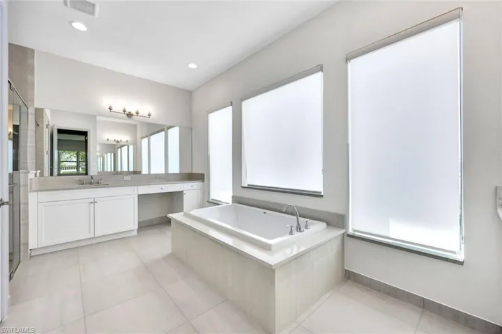 Primary Bathroom featuring shower with separate bathtub, tile patterned flooring, and one of two vanities