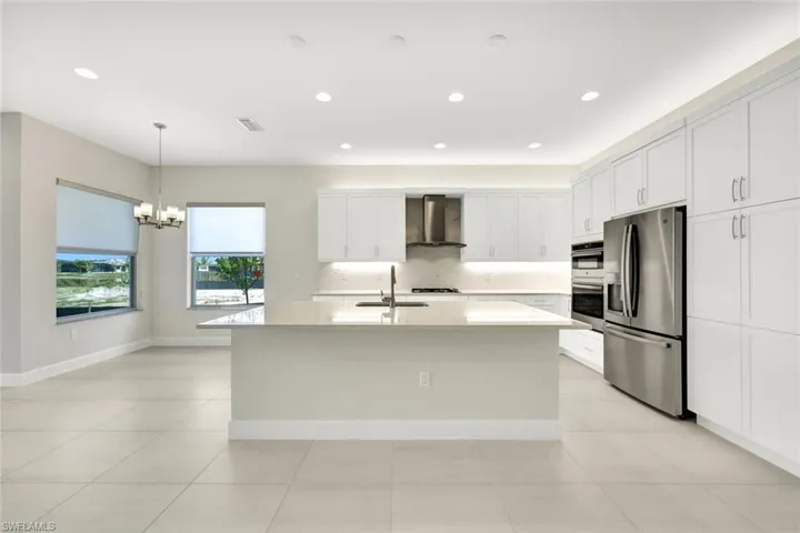 Kitchen featuring appliances with stainless steel finishes, white cabinetry, wall chimney exhaust hood, a center island with sink, and Breakfast area with chandelier