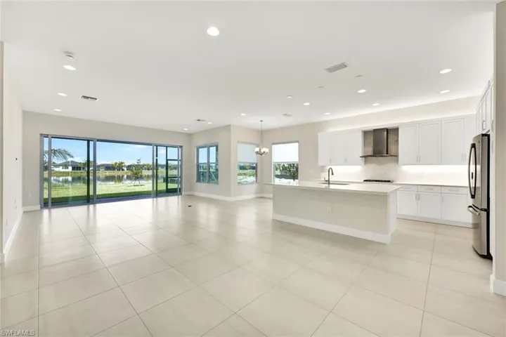 Kitchen with stainless steel fridge, wall chimney exhaust hood, a kitchen island with sink, and plenty of natural light.  Also views of Dining, Breakfast area, and Living Room