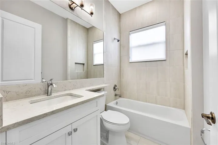 Full bathroom on first floor featuring tiled shower / bath, vanity, toilet, and tile patterned floors