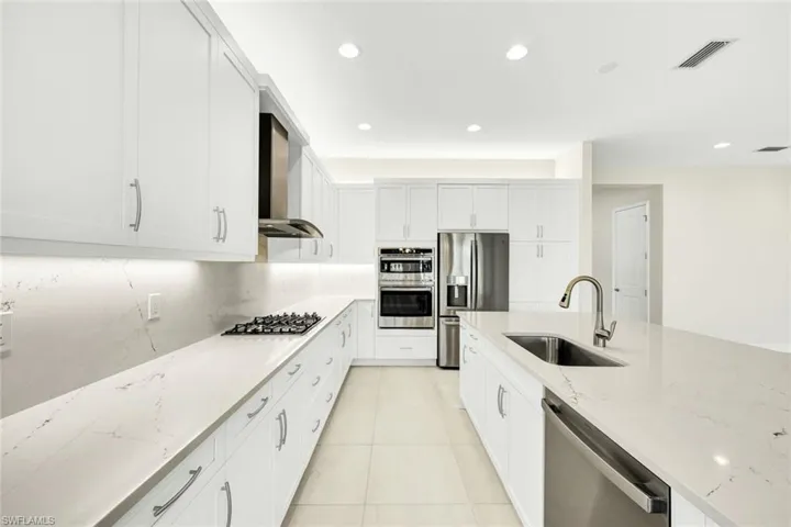 Kitchen featuring light stone counters, sink, wall chimney range hood, white cabinetry, and stainless steel appliances