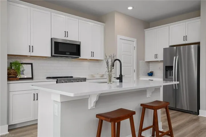 Kitchen featuring light hardwood / wood-style floors, a kitchen island with sink, tasteful backsplash, white cabinetry, and stainless steel appliances