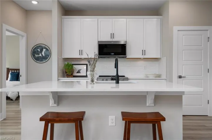 Kitchen featuring a center island with sink, light hardwood / wood-style floors, white cabinets, and tasteful backsplash