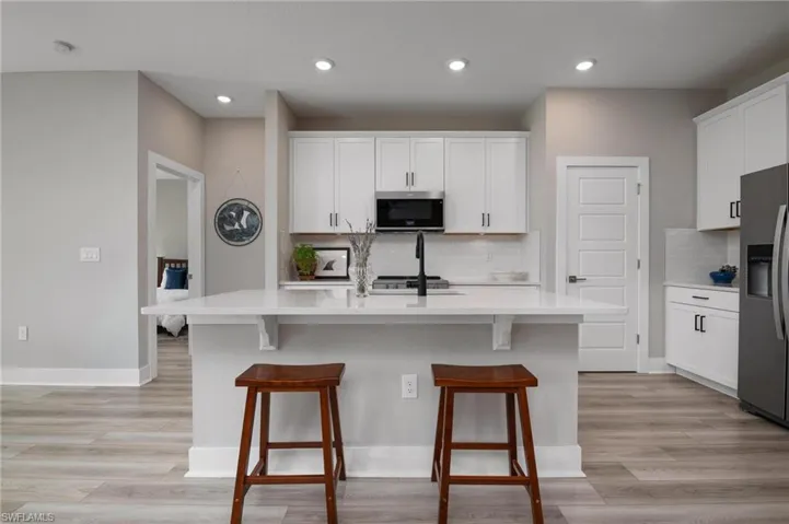 Kitchen with light hardwood / wood-style floors, tasteful backsplash, stainless steel appliances, a center island with sink, and white cabinets