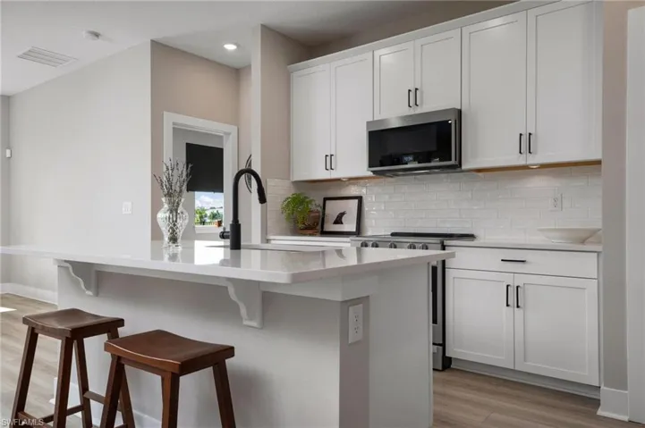 Kitchen with light wood-type flooring, backsplash, white cabinets, a kitchen bar, and appliances with stainless steel finishes