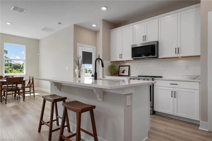 Kitchen with light hardwood / wood-style flooring, backsplash, white cabinetry, appliances with stainless steel finishes, and a center island with sink