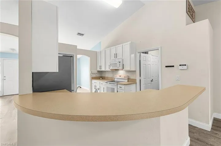 Kitchen featuring arched walkways, white appliances, light wood-style floors, white cabinets, and light countertops