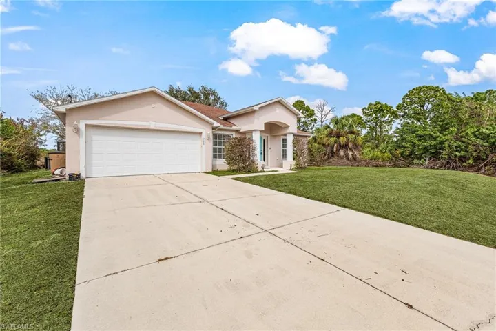 Single story home featuring a front lawn, stucco siding, driveway, and an attached garage