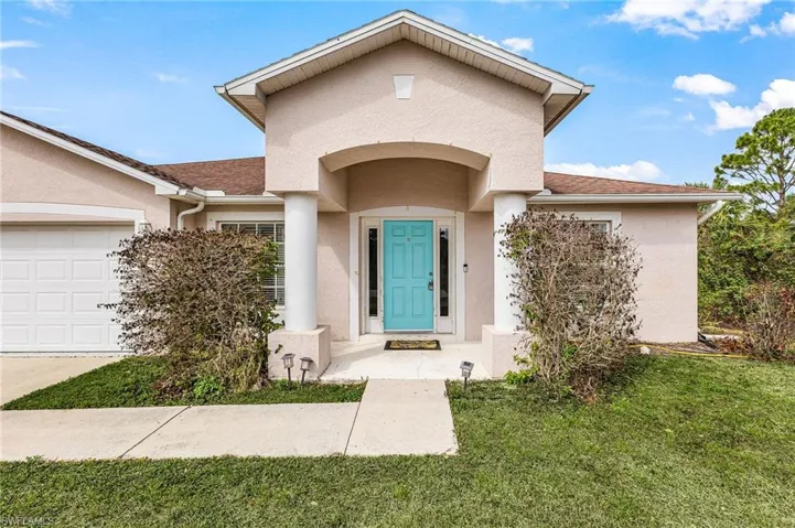 Doorway to property with stucco siding, a yard, a shingled roof, and an attached garage