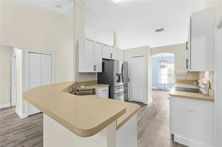 Kitchen with arched walkways, a peninsula, light countertops, stainless steel refrigerator with ice dispenser, and lofted ceiling