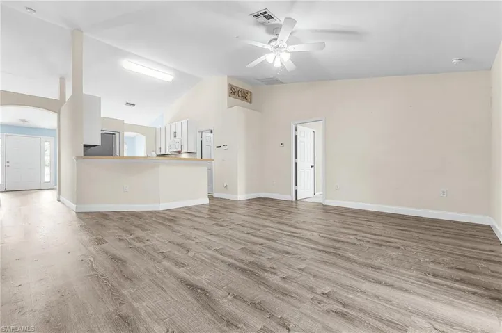 Unfurnished living room featuring a ceiling fan, light wood-style floors, vaulted ceiling, and arched walkways