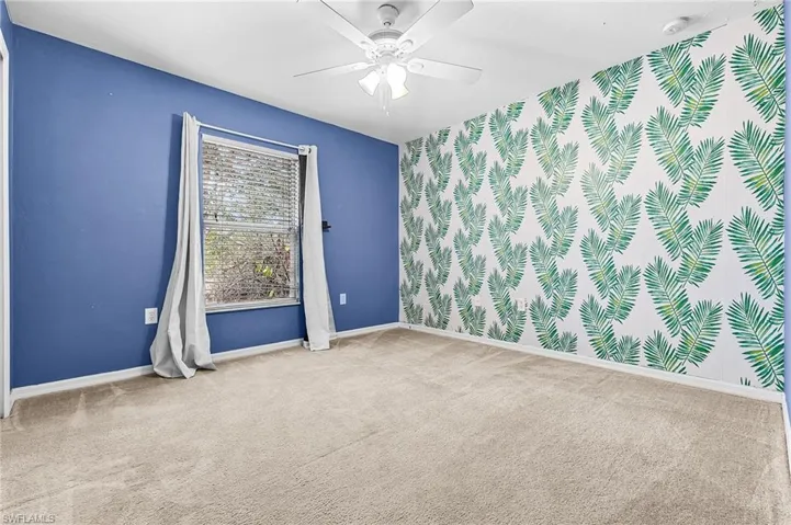 Carpeted spare room featuring ceiling fan, an accent wall, and wallpapered walls