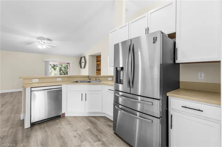 Kitchen featuring stainless steel appliances, vaulted ceiling, light countertops, light wood-style flooring, and white cabinets