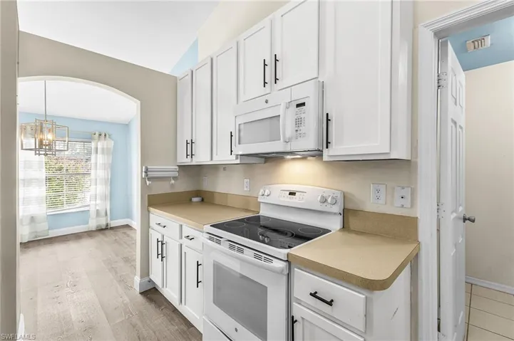 Kitchen featuring white appliances, white cabinets, light countertops, a chandelier, and lofted ceiling