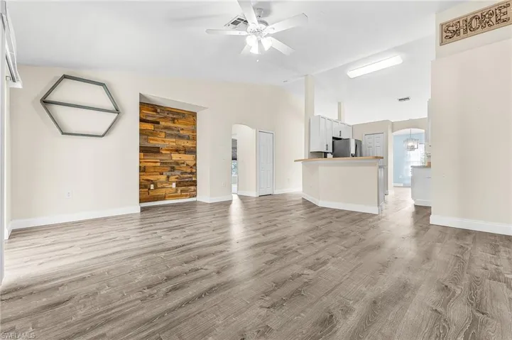 Unfurnished living room featuring arched walkways, ceiling fan, lofted ceiling, and light wood-style floors