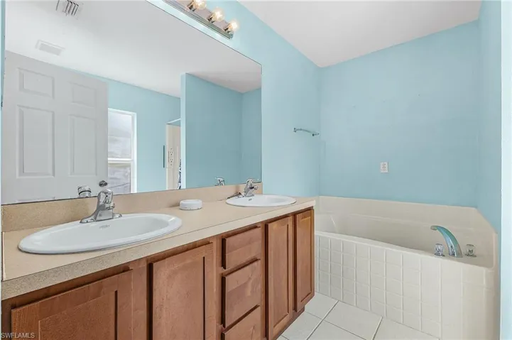 Full bath with double vanity, a bath, and light tile patterned floors