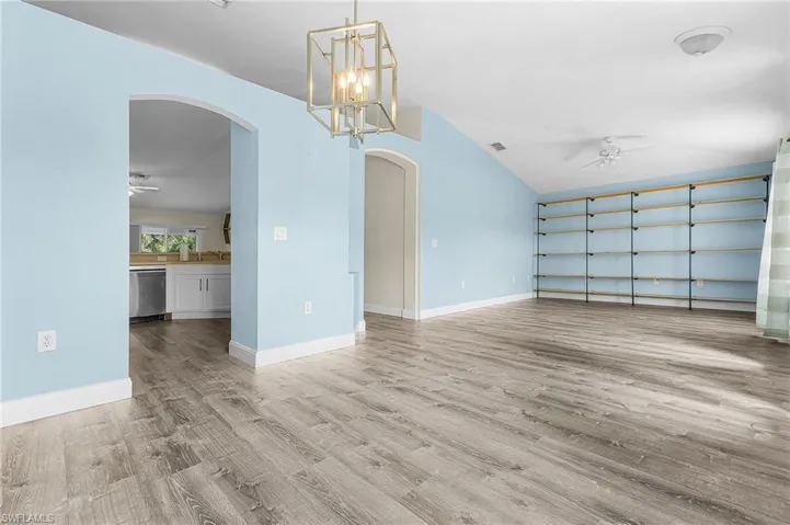 Unfurnished dining area with ceiling fan, arched walkways, a chandelier, lofted ceiling, and light wood-style floors