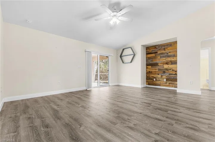 Unfurnished room with a ceiling fan, vaulted ceiling, dark wood-type flooring, and wood walls