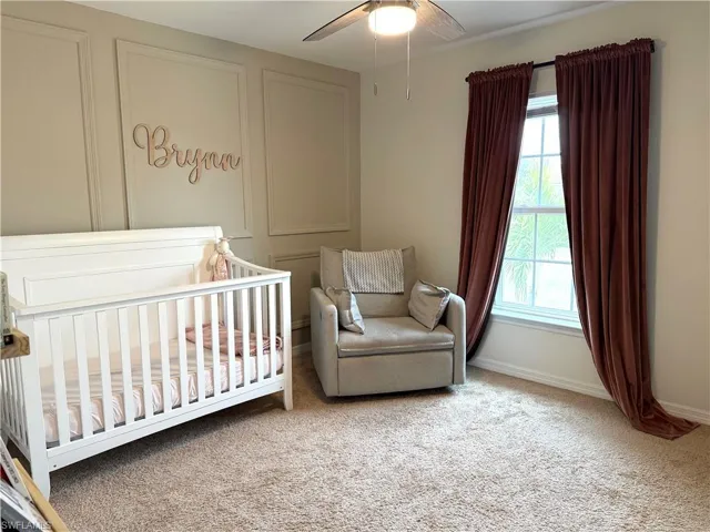 Carpeted bedroom featuring ceiling fan, multiple windows, and a crib