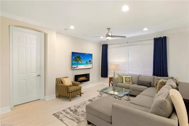 Living area with crown molding, wood finished floors, ceiling fan, a warm lit fireplace, and recessed lighting