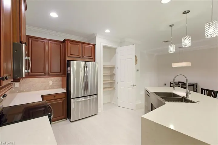 Kitchen featuring stainless steel appliances, decorative light fixtures, ornamental molding, backsplash, and light stone countertops