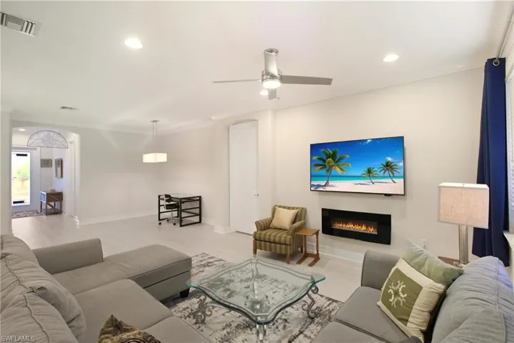 Living room with wood finished floors, a warm lit fireplace, recessed lighting, ceiling fan, and ornamental molding