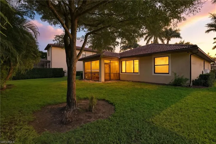 Rear view of property featuring a sunroom, stucco siding, a tiled roof, and a yard
