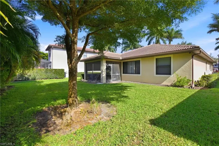 Rear view of property with a lawn, a tiled roof, stucco siding, and a sunroom
