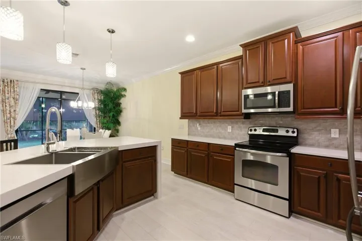 Kitchen with stainless steel appliances, pendant lighting, ornamental molding, a chandelier, and backsplash