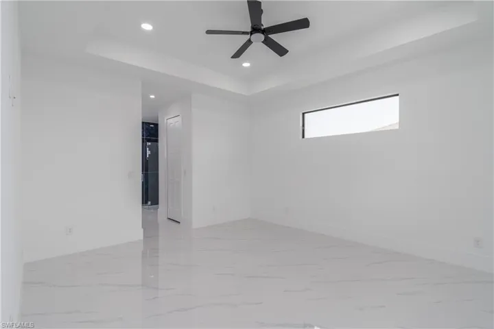 Spare room with a tray ceiling, light tile flooring, and ceiling fan