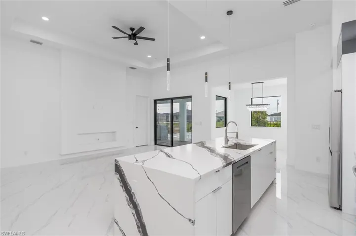Kitchen with a center island with sink, white cabinets, decorative light fixtures, ceiling fan, and a raised ceiling