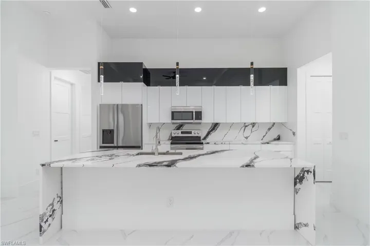 Kitchen with white cabinetry, light tile flooring, light stone counters, and stainless steel appliances