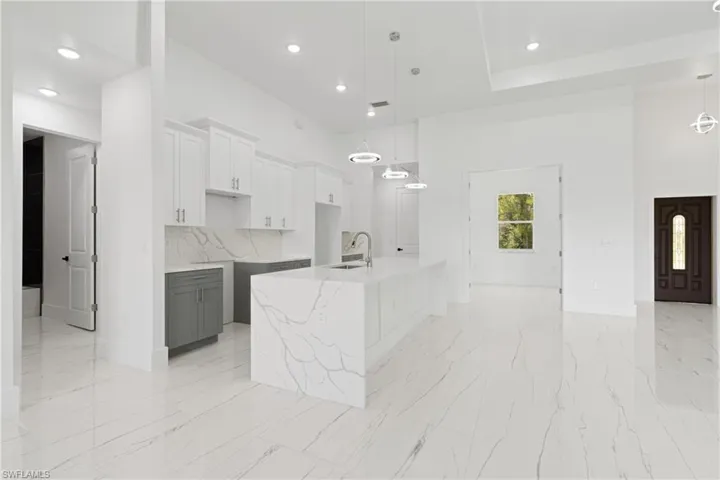 Kitchen with light tile patterned floors, a center island with sink, white cabinets, decorative light fixtures, and sink